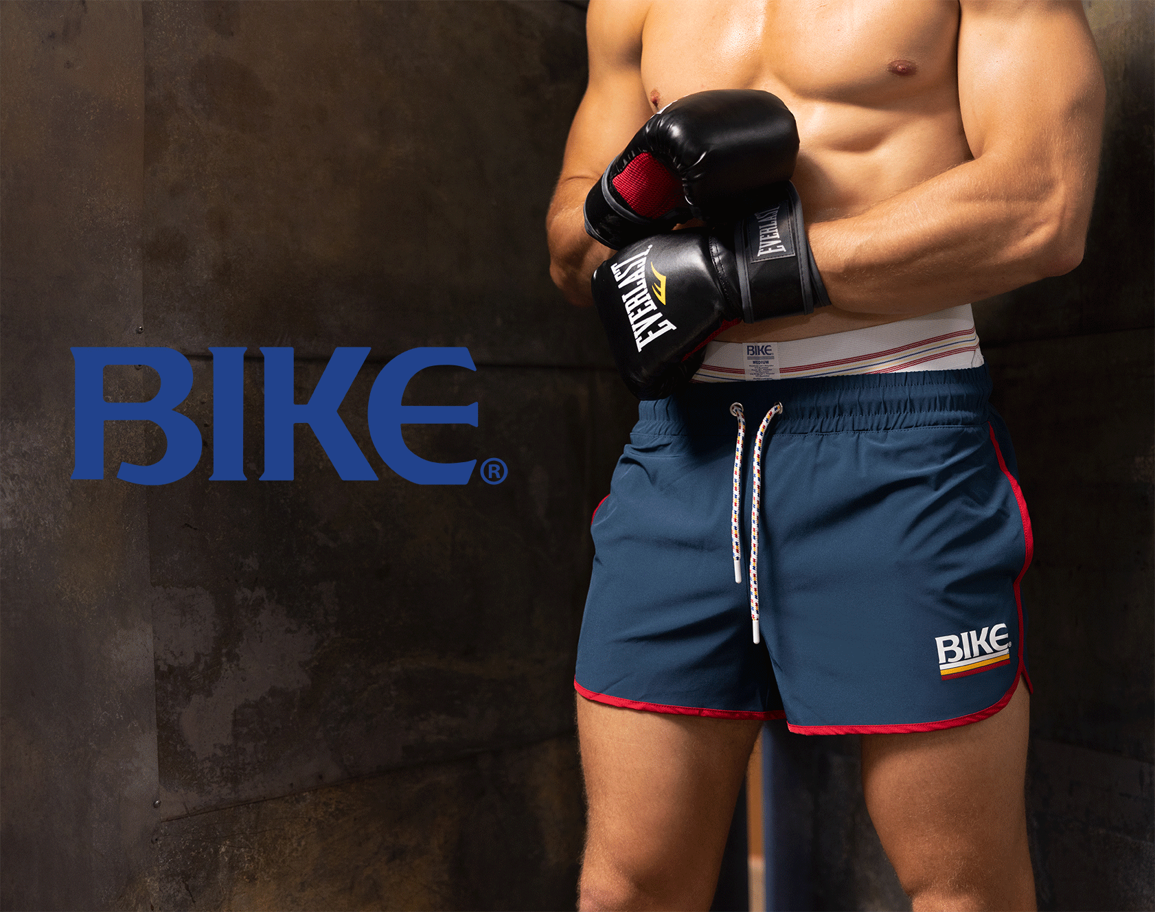 Male model wearing BIKE brand athletic shorts and boxing gloves, representing the brand's athletic apparel for men.